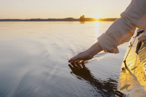 Slow traveler touching water from kayak during sunset