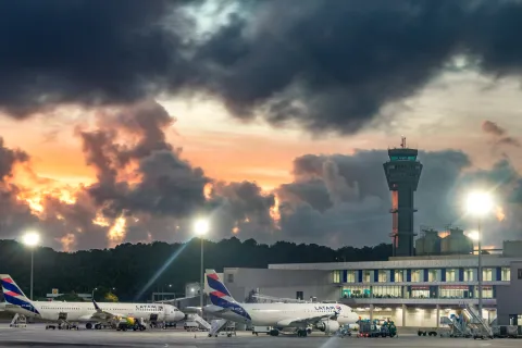 LATAM Airbus A320 parked at gate at Salvador Bahia Airport with the air traffic control tower in the background at dawn