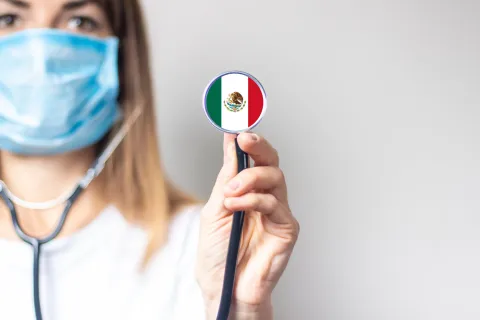 female doctor in a medical mask holds a stethoscope on a light background. Added flag of Mexico. 