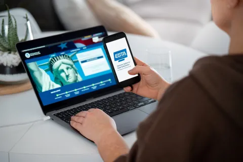 Woman holding smartphone with ESTA Electronic System for Travel Authorization logo, filling form to travel to the United States under the Visa Waiver Program 