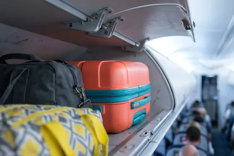 Carry-on luggage in an airplane overhead bin with suitcases and travel bags during boarding