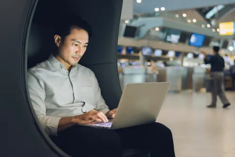 Asian man working on laptop in airport lounge