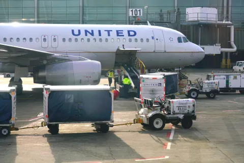A United Airlines jet parked at Gate 101 at Newark Liberty International Airport with baggage carts and a tug on the tarmac