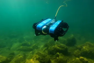 A tethered underwater ROV hovering above a rocky lakebed