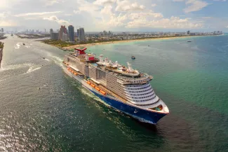 Large passenger cruise ship departing Miami port at sunset. Scenic view of South Beach waterfront with high-rise hotels and residential towers.