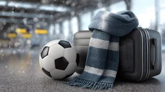 Football travel concept with soccer ball, suitcase, and winter fan scarf in an airport terminal background.