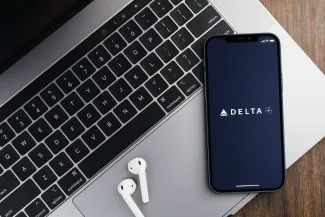 Delta Airlines app on the smartphone screen on wooden background with a computer beside it.