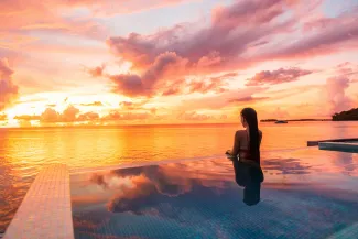 Paradise sunset idyllic vacation woman silhouette swimming in infinity pool looking at sky reflections over ocean dream. Perfect amazing travel destination