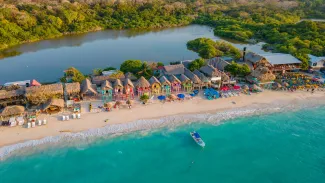 Aerial view of Playa Blanca, Baru, with crystal clear waters, white sandy beach, colorful huts, and lush greenery
