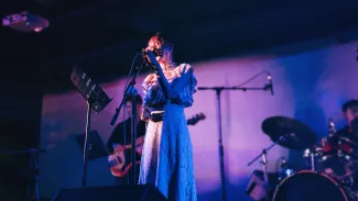 A female vocalist singing on stage with a live band under blue and purple concert lighting