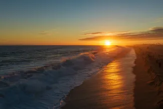 Golden sunset over Newport Beach, California, with powerful Pacific Ocean waves rolling toward the sandy shoreline