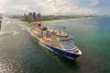 Large passenger cruise ship departing Miami port at sunset. Scenic view of South Beach waterfront with high-rise hotels and residential towers.