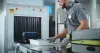 Airport Security Checkpoint: Security Officer Putting Suitcases and Personal Items in Trays on Conveyor Belt with X-ray Scanning. People Passing Through Metal Detector Gates. 