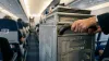 The metal catering service cart being pushed by a flight attendant inside a commercial airplane cabin.